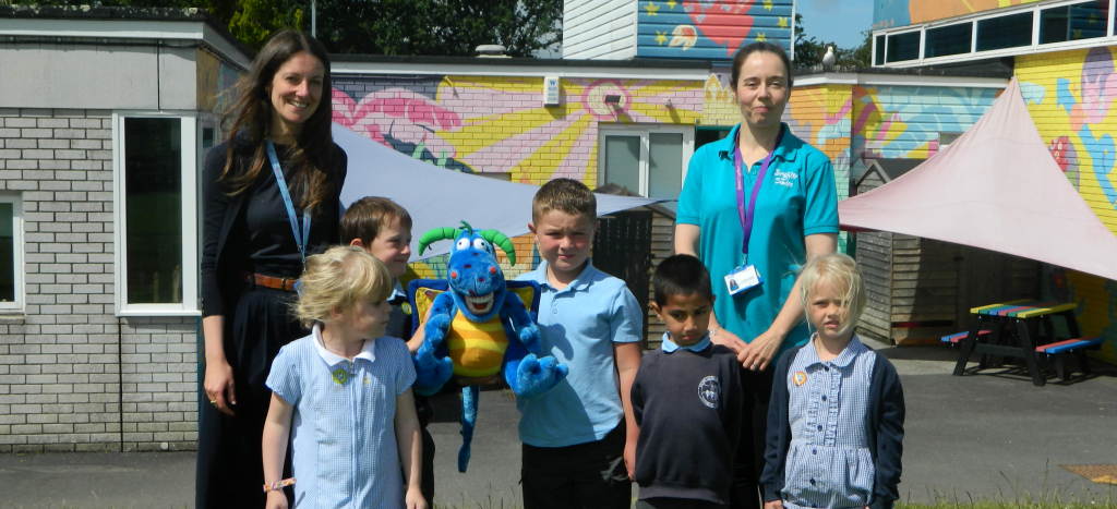 Adults and children in playground with cuddly toy dragon